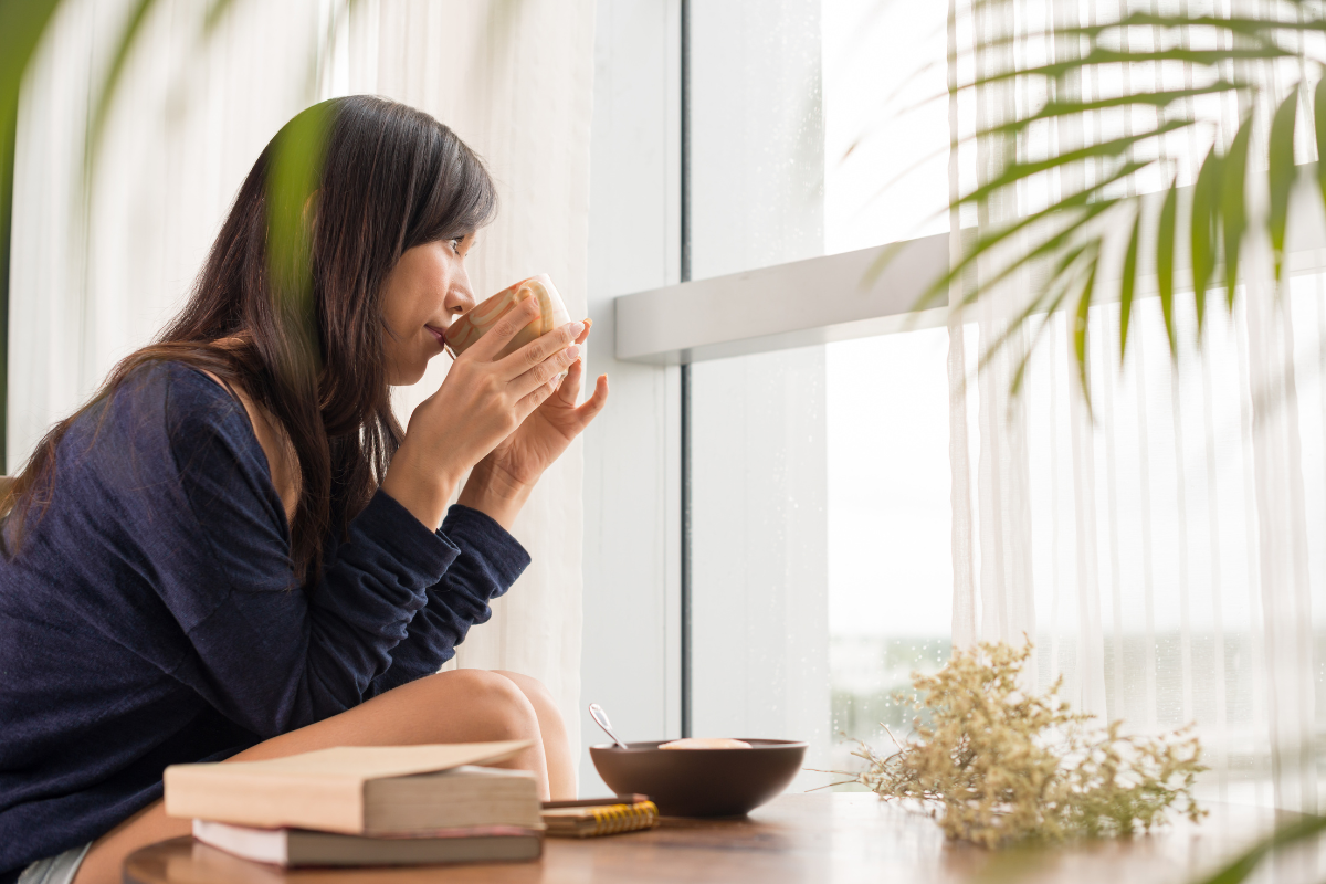 Woman enjoying tea in a calm home environment after creating more clarity and breathing room in her space.