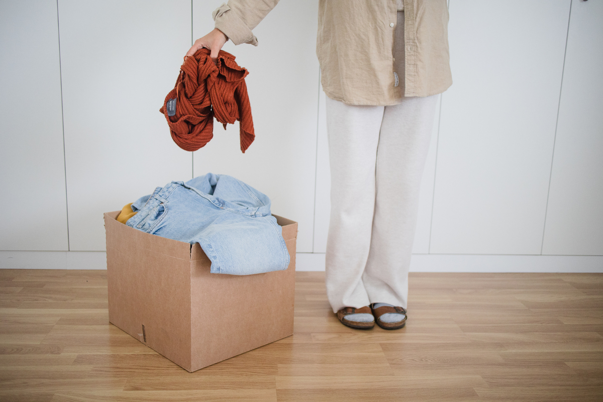 Person editing clothing and placing unwanted pieces into a donation box before moving.