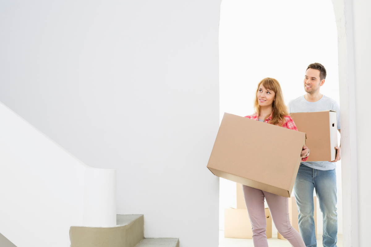 Couple carrying moving boxes into a bright new home as they begin settling into their space.