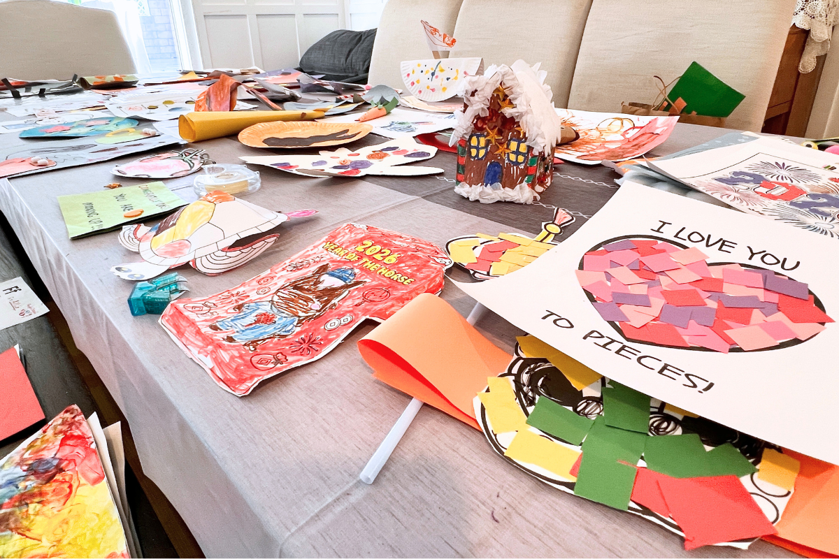 Children’s artwork spread across a table during the editing process, including drawings, crafts, and school projects
